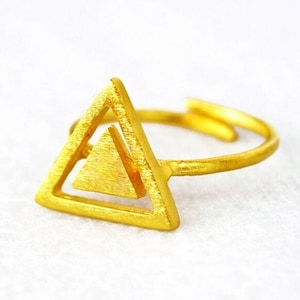 Puede incluir: Un anillo de color dorado con un diseño de doble triángulo. El anillo está hecho de metal y tiene una forma simple y geométrica.