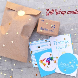 Puede incluir: Una bolsa de regalo de papel marr&oacute;n con una pegatina de estrella dorada, una peque&ntilde;a caja marr&oacute;n con el texto "Bubble Box" y una tarjeta azul y blanca con el texto "&iexcl;Gracias!" y un logotipo que dice "Bubble Box Joyer&iacute;a hecha a mano y dise&ntilde;os personalizados".