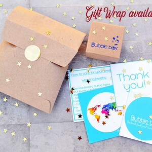 May include: A brown paper gift bag with a gold sticker and a small brown box with the text "Bubble Box" on it. The image also includes a blue card with the text "Thank you!" and a world map with rainbow colors. The text "Gift Wrap available!" is written in red at the top of the image.
