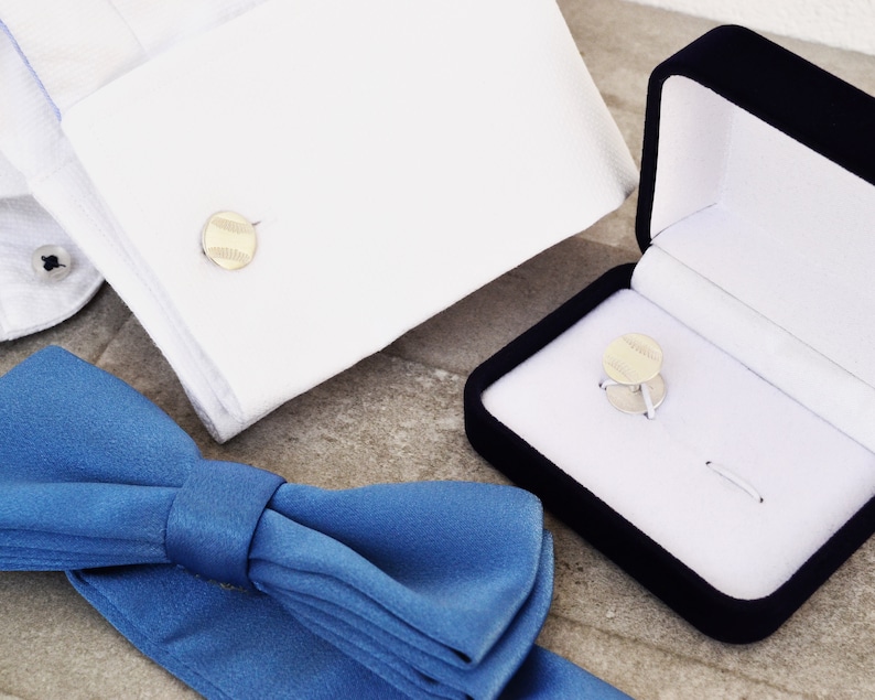 May include: A blue bow tie, a white dress shirt cuff with a gold cufflink, and a black velvet box with a gold cufflink inside.