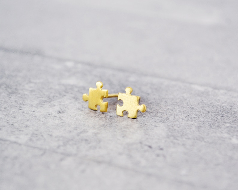 May include: A pair of gold-toned puzzle piece earrings. The earrings are small and delicate, and they are perfect for adding a touch of whimsy to any outfit.