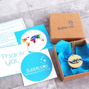 May include: A gold necklace with a pendant shaped like the island of Indonesia. The necklace is in a small brown box with blue tissue paper. The box has the words "Bubble box" printed on it.