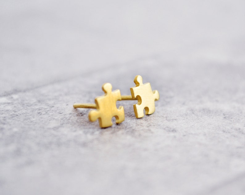 May include: A pair of gold-toned puzzle piece earrings. The earrings are small and delicate, and they are perfect for adding a touch of whimsy to any outfit.
