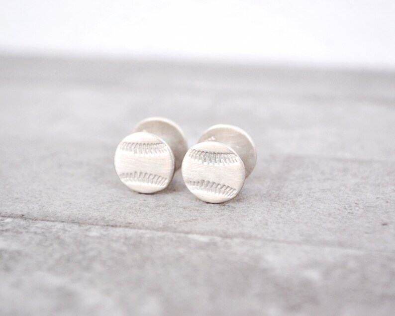 May include: A pair of silver cufflinks with a baseball design.