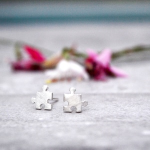 May include: A pair of silver puzzle piece earrings. The earrings are small and delicate, and they are perfect for everyday wear.