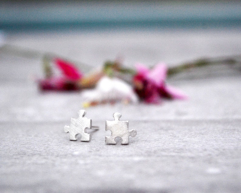 May include: A pair of silver puzzle piece earrings. The earrings are small and delicate, and they are perfect for everyday wear.