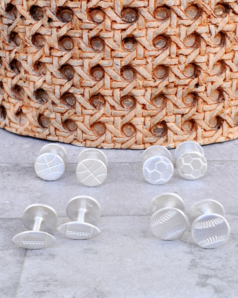 May include: Six pairs of silver cufflinks with different sports designs: basketball, soccer, football, and baseball.