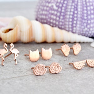 May include: A set of rose gold stud earrings featuring various designs, including flamingos, cats, strawberries, watermelon slices, and roses.