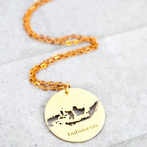 May include: A gold necklace with a pendant shaped like the outline of Indonesia. The pendant has the word "Indonesia" inscribed on it.