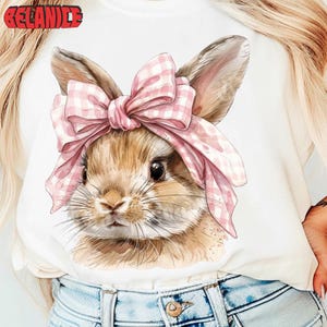 May include: White t-shirt featuring a watercolor illustration of a bunny wearing a pink gingham bow. The bunny has brown fur and large, dark eyes. The word "BELANICE" is printed in red letters at the top left.