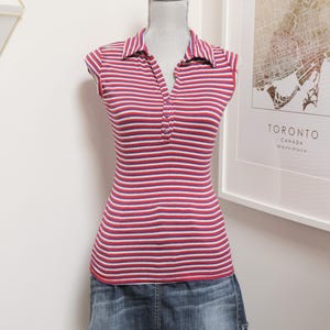 May include: A sleeveless polo shirt featuring horizontal stripes in red, white, and blue, with a collared neckline and a three-button placket, paired with a dark blue denim mini skirt that has a frayed hemline and a faded wash finish.