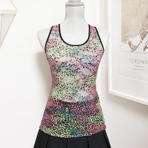 May include: A colourful athletic vest and black pleated skirt displayed on a mannequin. The vest features a vibrant leopard print in shades of pink, green, yellow, and black. The vest has a black trim.