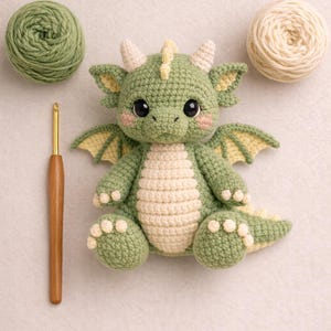 Puede incluir: Un drag&oacute;n de ganchillo hecho a mano en tonos verdes y crema, con peque&ntilde;as alas y cuernos. Un ganchillo y dos ovillos de lana en colores a juego se colocan cerca del drag&oacute;n. El drag&oacute;n tiene una expresi&oacute;n amigable.
