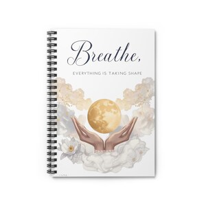 Puede incluir: Cuaderno de espiral blanco con la frase "Breathe, Everything is Taking Shape". El diseño incluye una luna dorada, manos y detalles florales en tonos dorados y blancos.