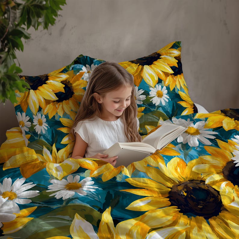 May include: A young person reading a book while nestled in a bed covered with a sunflower and daisy patterned duvet and pillowcase set. The bedding features large yellow sunflowers and white daisies against a teal background.