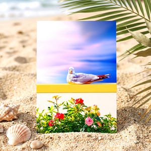 Puede incluir: Una impresión rectangular que muestra una gaviota descansando sobre una repisa amarilla contra un cielo azul y morado, sobre un jardín de rosas rojas, rosas y amarillas. La impresión se exhibe en una playa de arena con conchas.
