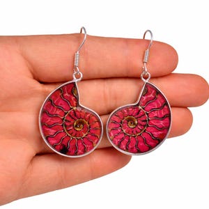 May include: Silver-coloured earrings with a striking red and gold spiral pattern, reminiscent of a nautilus shell's cross-section. The earrings have a hook fastening.