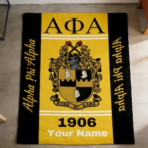 Op de afbeelding: Een rechthoekige zwarte, gele en gouden deken. De deken heeft de Griekse letters ΑΦΑ, een wapen en het jaar 1906. De woorden "Alpha Phi Alpha" staan verticaal op de linker- en rechterkant.