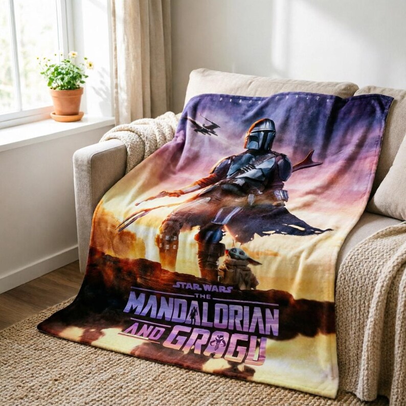 May include: A Star Wars themed blanket featuring The Mandalorian and Grogu against a sunset backdrop. The blanket displays the show's title in a stylized font. The color palette includes shades of purple, orange, and brown.