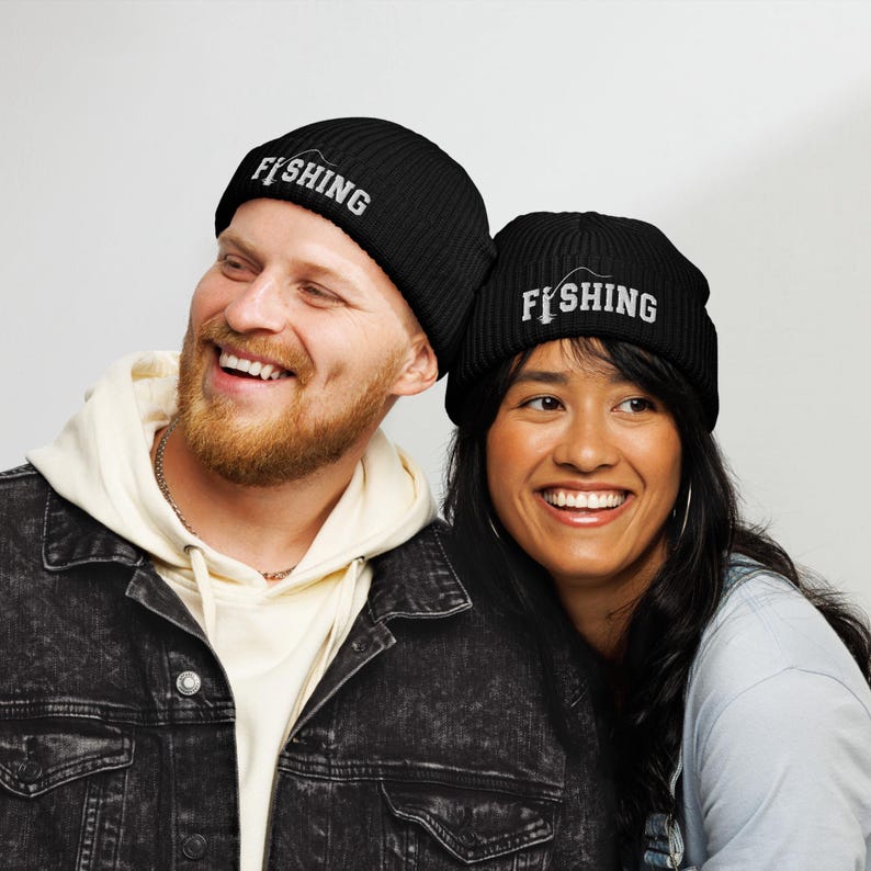 May include: Two black ribbed knit beanies featuring white embroidered text that reads FISHING, with the letter I replaced by a graphic of a fishing rod and line. The hats have a cuffed design and are made of a textured, thick knit material.
