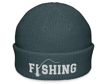 Puede incluir: Un gorro de punto gofrado en color verde azulado oscuro con dobladillo. En la parte frontal presenta un bordado blanco con el texto FISHING, donde la letra I se sustituye por el gráfico de una persona con caña.