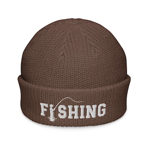 May include: A brown knit beanie with a cuffed brim featuring white embroidered text that reads FISHING, with the letter I replaced by a graphic of a person holding a fishing rod and line extending over the remaining letters.