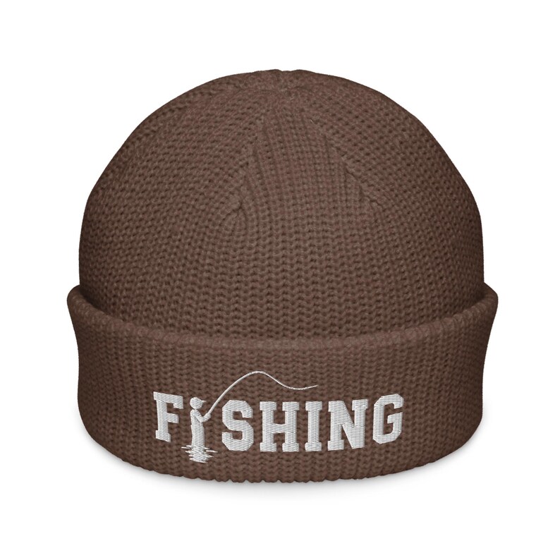 May include: A brown knit beanie with a cuffed brim featuring white embroidered text that reads FISHING, with the letter I replaced by a graphic of a person holding a fishing rod and line extending over the remaining letters.