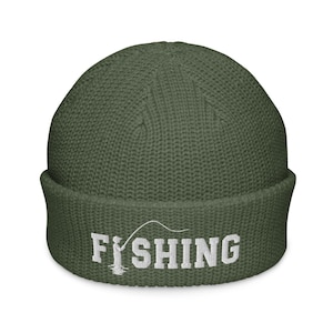 May include: An olive green knit beanie with a cuffed brim. The front features white embroidered text that reads FISHING, with the letter I replaced by a graphic of a person holding a fishing rod and line extending over the letters.