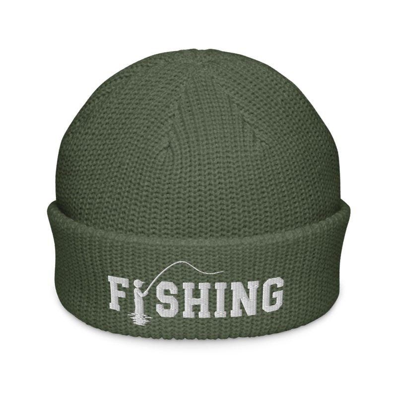 May include: An olive green knit beanie with a cuffed brim. The front features white embroidered text that reads FISHING, with the letter I replaced by a graphic of a person holding a fishing rod and line extending over the letters.
