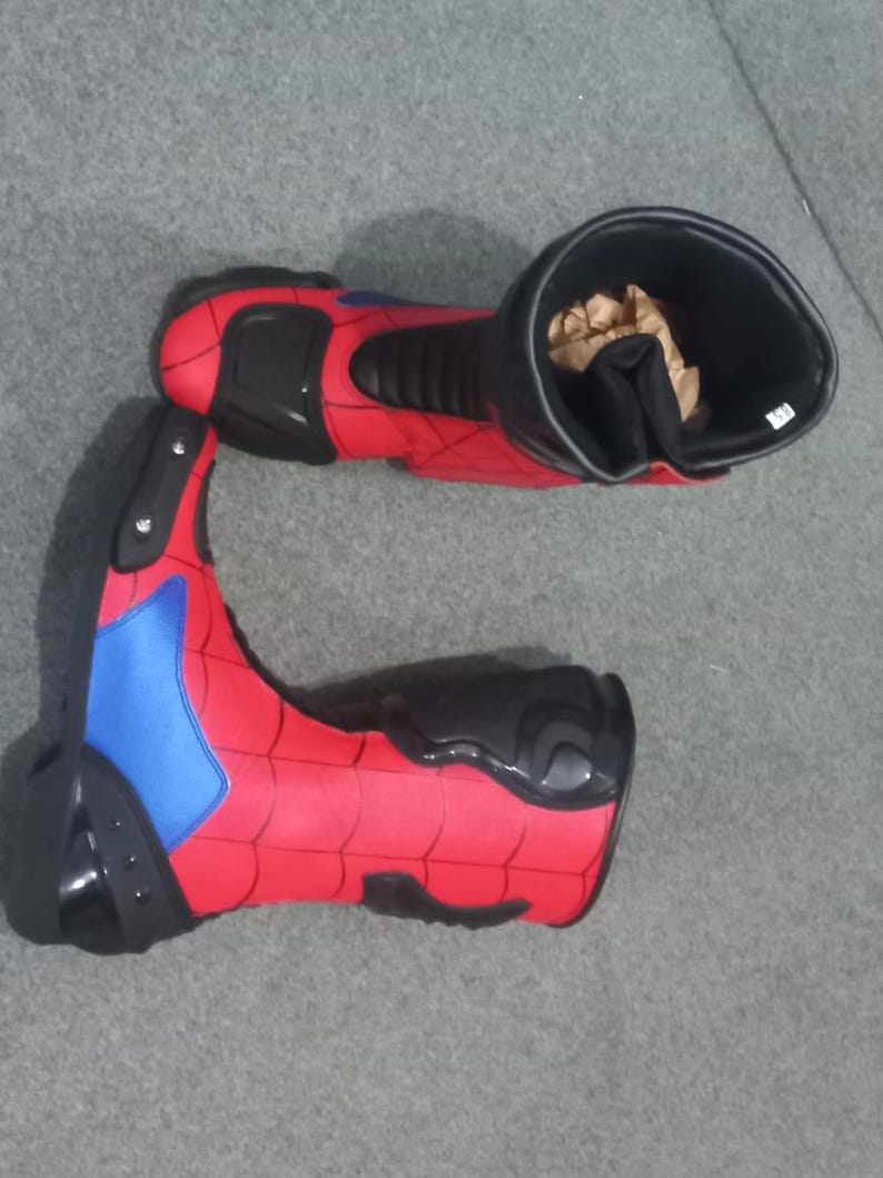 K&ouml;nnte beinhalten: Paar rote und schwarze Motorradstiefel mit blauem Akzent. Die Stiefel haben ein strukturiertes Design und Schutzelemente. Das Innere eines Stiefels ist sichtbar und enth&auml;lt braunes Verpackungsmaterial. Die Stiefel sind auf Sicherheit und Leistung ausgelegt.