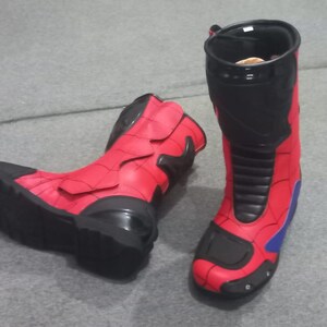 K&ouml;nnte beinhalten: Paar rot-schwarze Stiefel mit Superhelden-Thema. Die Stiefel haben ein hoch geschnittenes Design mit rotem Obermaterial, schwarzen Akzenten und blauen Details. Die Stiefel sind aus synthetischem Material und scheinen neu zu sein.