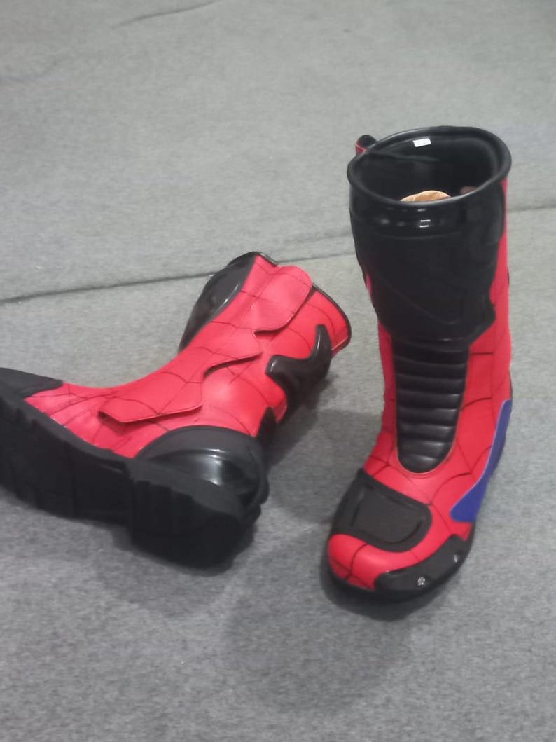 K&ouml;nnte beinhalten: Paar rot-schwarze Stiefel mit Superhelden-Thema. Die Stiefel haben ein hoch geschnittenes Design mit rotem Obermaterial, schwarzen Akzenten und blauen Details. Die Stiefel sind aus synthetischem Material und scheinen neu zu sein.
