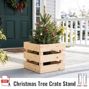 Puede incluir: Un soporte de madera cuadrado en forma de caja con listones horizontales, fabricado en madera natural de color claro. La caja contiene un pequeño árbol de hoja perenne decorado con esferas rojas y doradas y luces.