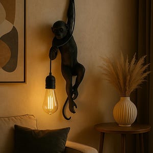 Puede incluir: Una lámpara de pared con forma de mono gris oscuro cuelga de un cable negro, sosteniendo una bombilla. La lámpara está montada en una pared beige, con un sofá y una mesa auxiliar en primer plano. Un jarrón con plantas secas está sobre la mesa auxiliar.