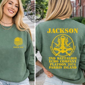 May include: Green sweatshirt with "PROUD DAD" and an American flag design on the front. The back features the name "JACKSON" and military insignia with text: "2ND BATTALION ECHO COMPANY PLATOON 2074 PARRIS ISLAND".