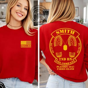 May include: Red sweatshirt with a yellow American flag and the text "PROUD MOM" on the front. The back features the name "SMITH", military insignia, and text including "2ND BN FOX COMPANY" and "PLATOON 1047 PARRIS ISLAND".