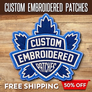 May include: A blue and white embroidered patch in the shape of a maple leaf. The patch features the words "CUSTOM EMBROIDERED PATCHES" in white lettering. The patch is set against a wooden background.