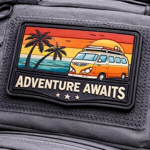 May include: A gray backpack with a rectangular patch featuring a colorful illustration of a vintage van on a beach with palm trees and the text "ADVENTURE AWAITS". The patch has a black border and three stars.