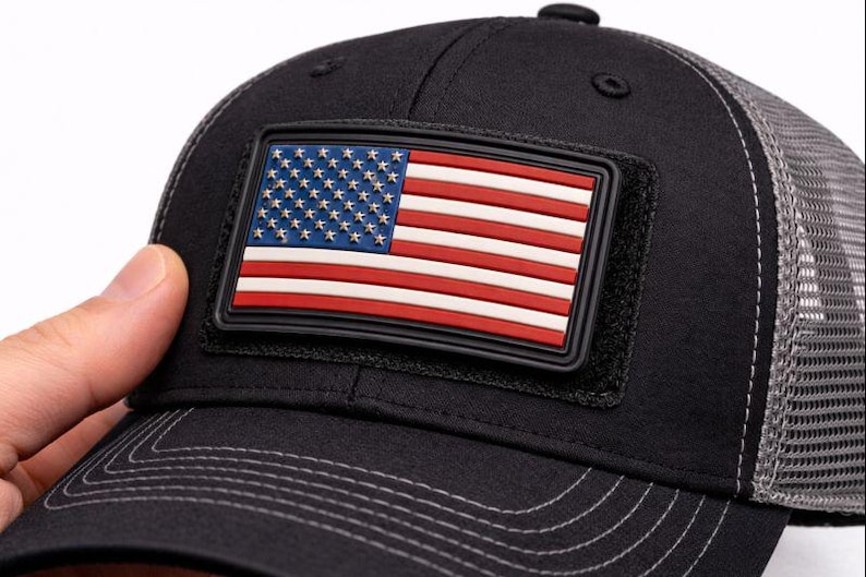 May include: Black baseball cap with a mesh back and a rectangular patch featuring the American flag. The flag design includes red and white stripes and a blue field with white stars. The cap is made of a durable fabric.