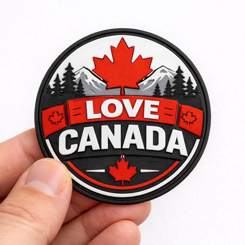 May include: A round, black, white, and red patch with the words "LOVE CANADA" in white. The design includes a red maple leaf, mountains, and pine trees. The patch is held by a hand.