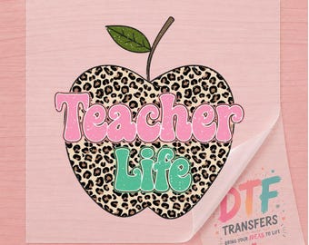 May include: A square DTF transfer sheet featuring a large apple shape with a leopard print pattern. The word Teacher is written in pink letters across the top, and the word Life is written in green letters below. A green leaf sits on the stem.