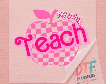 May include: A clear DTF transfer sheet featuring a pink and light pink checkered apple graphic with the text My job is... and the word Teach in a bold pink font. A corner of the sheet is peeled back to reveal a logo with the text DTF TRANSFERS.
