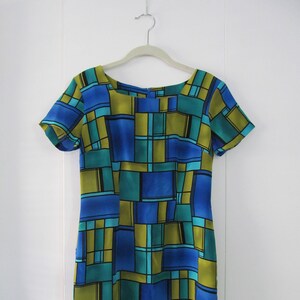 May include: A short-sleeved dress with a geometric pattern in shades of blue, green, and yellow. The dress has a scoop neckline and a straight silhouette.