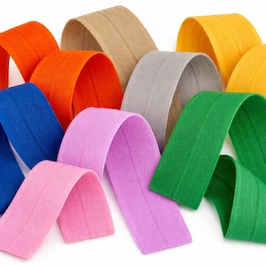 Puede incluir: Una colección de bandas elásticas coloridas en varios tonos, incluyendo naranja, azul, rosa, verde y amarillo. Las bandas están dispuestas en formas curvas, mostrando su flexibilidad y textura. Ideal para proyectos de manualidades o costura.