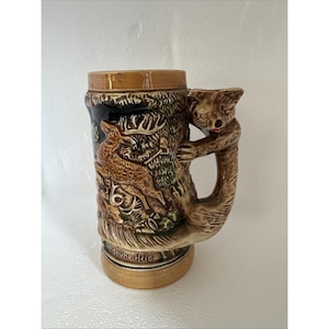 以下が含まれることがあります： 詳細なレリーフデザインのセラミック製ビールジョッキ。ジョッキは、茶色のクマのハンドルと鹿のいる森のシーンが特徴です。ベースには「Grüne Heid」と書かれています。色は茶色、タン、黒です。