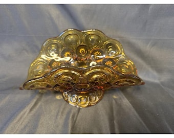 May include: A semi-circular amber glass bowl featuring a raised moon and star pattern across its surface. The bowl has a scalloped edge and sits on a circular pedestal base, showcasing a translucent, warm brown colour throughout the glass.