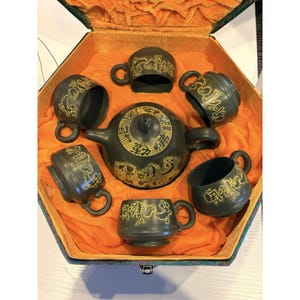 May include: A dark green tea set with gold accents, including a teapot and six cups, displayed in a hexagonal box with orange lining. The tea set features dragon motifs and Chinese characters.