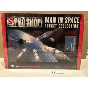May include: A model kit box for the "Man in Space Rocket Collection" with illustrations of rockets in space. The box has the "AMT ERTL PRO SHOP" logo and includes the scale 1:200. The background shows Earth and other celestial bodies.