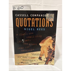 Könnte beinhalten: Ein Buch mit dem Titel "Cassell Companion to Quotations" von Nigel Rees. Das Cover zeigt ein Zitat über einen kleinen Schritt für den Menschen und einen riesigen Sprung für die Menschheit, mit einem Astronauten auf dem Mond. Das Buch ist schwarz mit orangefarbenen Buchstaben.