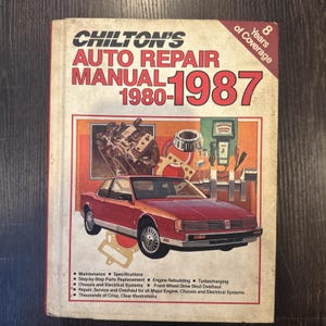 Puede incluir: Un manual de reparación de automóviles Chilton's vintage de 1980-1987, con una ilustración de un coche rojo en la portada. El manual incluye información sobre mantenimiento, reconstrucción de motores y sistemas eléctricos. La portada indica "8 Years of Coverage".